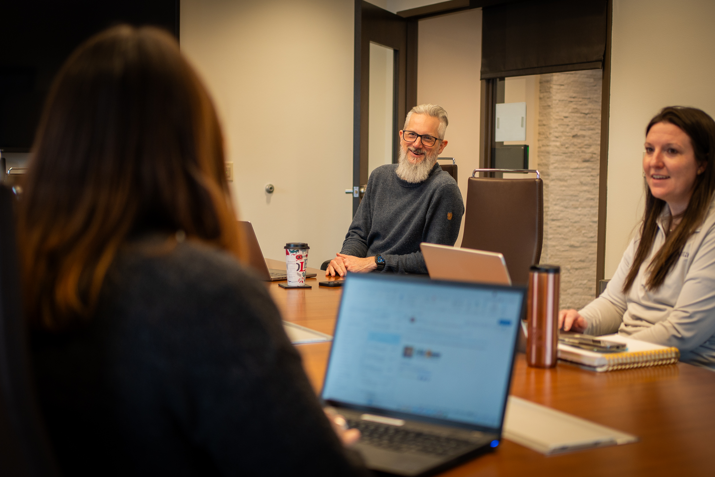 People sitting around a table with laptops. A laptop screen is in the foreground.