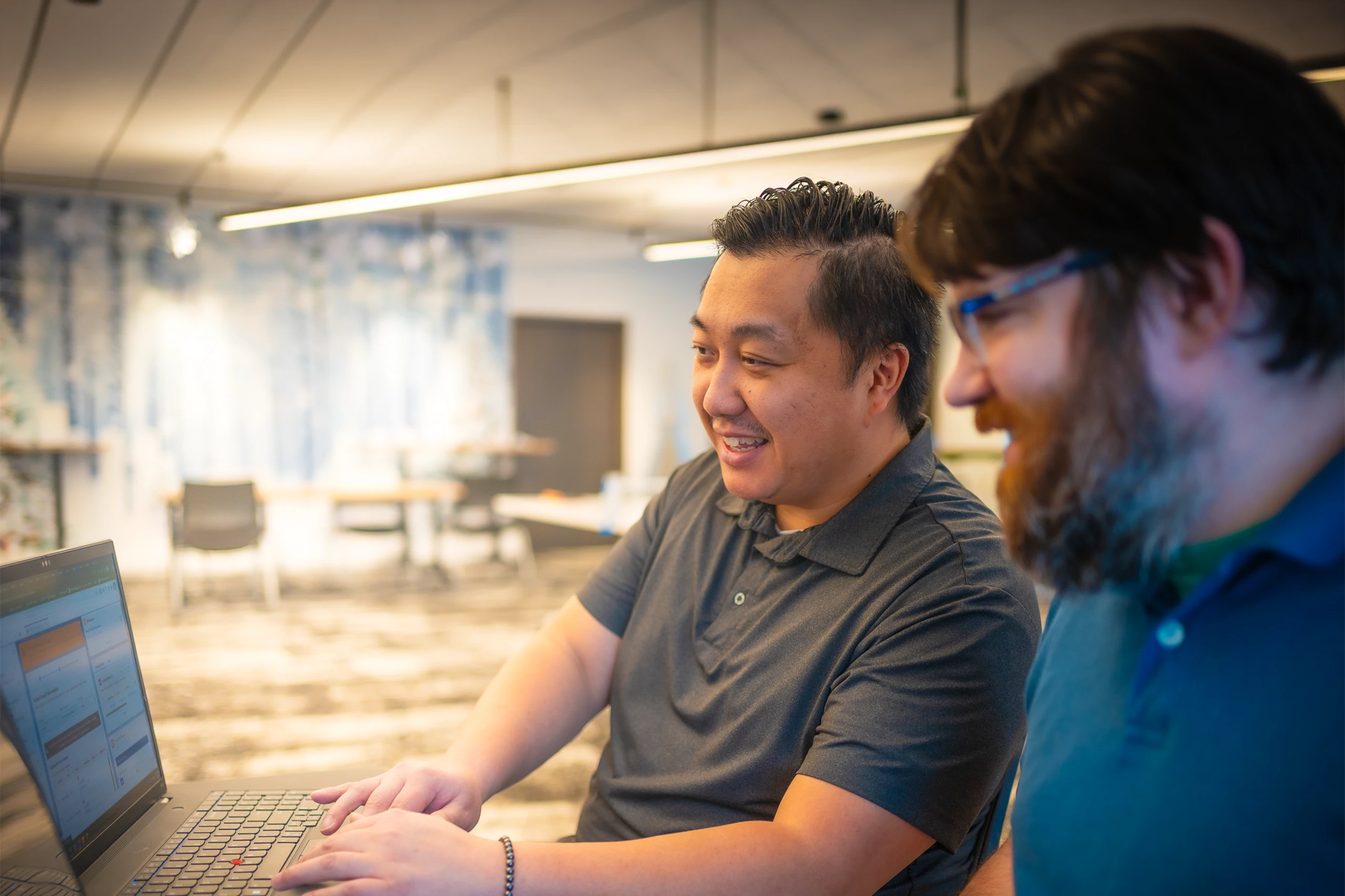 Two smiling men sitting at a laptop workstation.