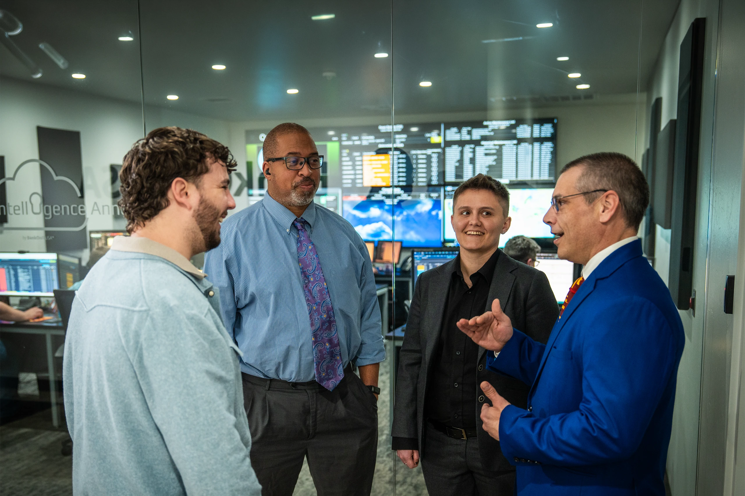 Group of smiling people listening to a man speak in an office setting.