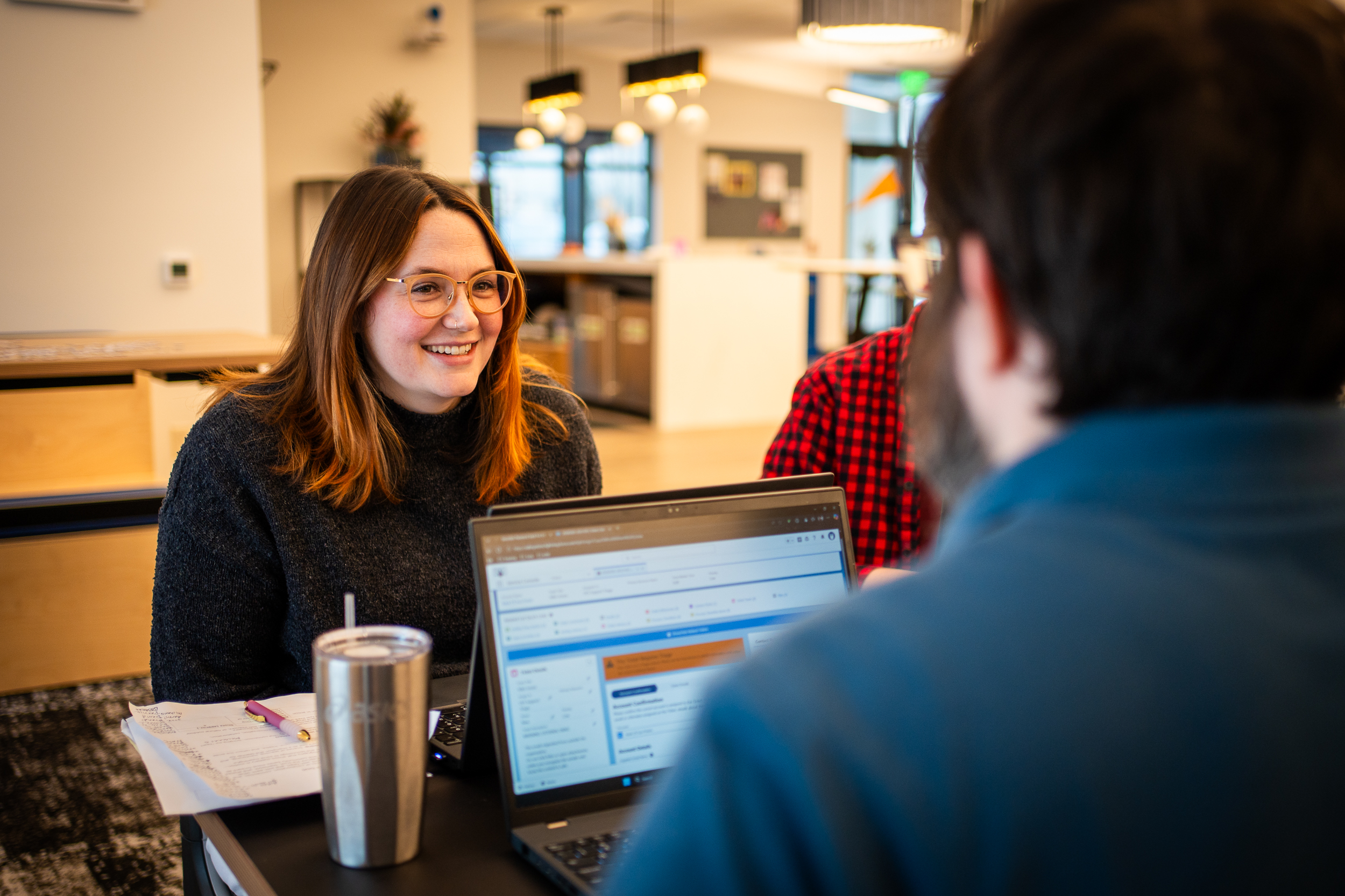Smiling woman facing a man on a laptop.
